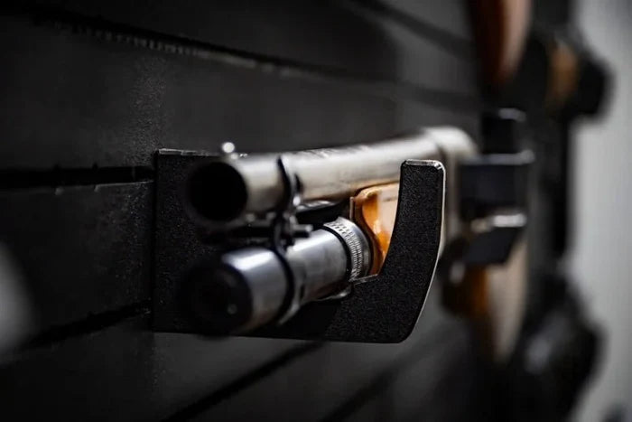 Close-up of a Tactical Walls MWHRACKRS ModWall rack holding the receiver of a shotgun, showing the rack's black HDPE curved profile that safely supports metal barrel and receiver components